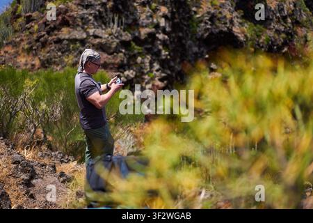 Man operating a drone controller among endemic scrub on a volcanic hillside near Masca in the Teno massif Stock Photo