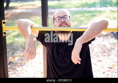 Relaxed man leaning on bar. Bearded individual enjoying sunlight break. Exhausted man relaxing with eyes closed in sunlight. Peaceful scene of tired man resting with eyes shut in sunlight Stock Photo