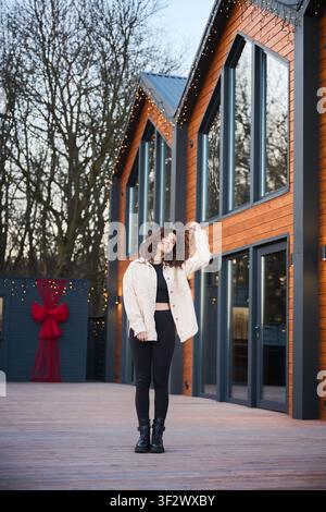 Young woman in casual outfit walking by modern house facade, highlighting independence, wellbeing, travel lifestyle and contemporary design Stock Photo