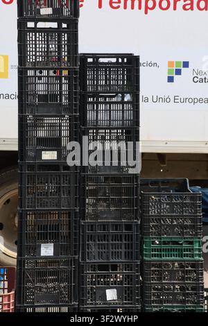 Viladecans, Spain - July 20, 2026: Black and green plastic storage crates stacked together during street market operations. Stock Photo