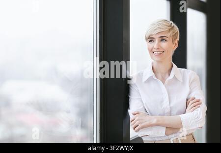 Joyful Lady Crossing Hands Standing Near Panoramic Window In Office Stock Photo