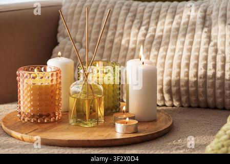 Group of burning candles and a reed diffuser sitting on a wooden tray, creating a cozy and relaxing atmosphere in a home interior, promoting wellness Stock Photo