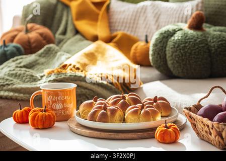 Warm and inviting hygge comfort setting featuring pumpkin-shaped bread buns on a plate, an orange mug with hot tea, and decorative fabric pumpkins on Stock Photo