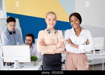 Portrait of female call centre operators smiling and looking at camera during coffee break at open space office Stock Photo