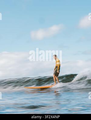 ALA MOANA BOWLS, HONOLULU, HAWAII - APRIL 1, 2022: A man in a gold rash guard rides poised on an orange longboard. Stock Photo
