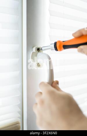 Close up of a handyman using an orange screwdriver to repair or replace a white plastic window handle Stock Photo