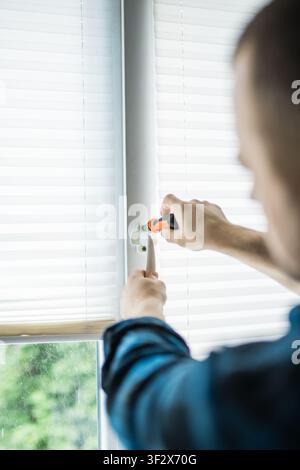 Man in a blue plaid shirt using a screwdriver to fix or adjust a white plastic window handle Stock Photo
