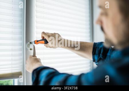 Man in a blue plaid shirt using a screwdriver to fix or adjust a white plastic window handle Stock Photo