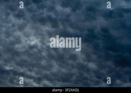 Dramatic dark storm clouds filling the sky texture background. Dense layer of dark grey and blue overcast clouds in a stormy sky creating a dramatic c Stock Photo