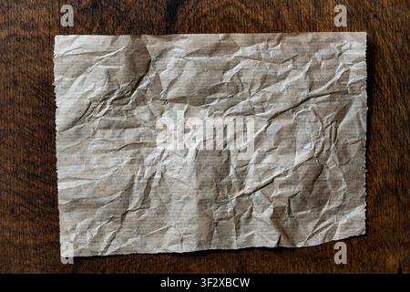 Crumpled piece of brown kraft paper on dark wooden background. Top view mockup of single wrinkled blank sheet of parchment paper placed on rustic dark Stock Photo