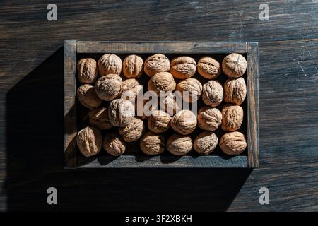 Walnuts in wooden box on dark background, close up. Top view of whole walnuts in shells inside rustic wooden frame on dark table. Healthy organic snac Stock Photo