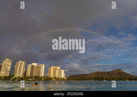 WAIKIKI, HONOLULU, HAWAII - MAY 3, 2022: A rainbow arcs over the Waikiki hotels and the Diamond Head crater seen from the water. Stock Photo