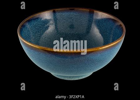 High-resolution close-up of a blue glazed ceramic bowl with a speckled texture and warm brown rim, photographed against a black background for product Stock Photo