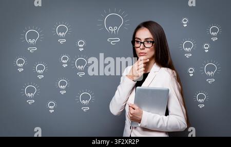 Pensive business lady with digital tablet surrounded by light bulbs Stock Photo