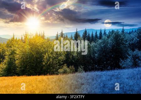 mountain landscape of ukraine. day meet night. sun and moon over alpine grassy meadow and deciduous forest on the hill. equinox nature background for Stock Photo