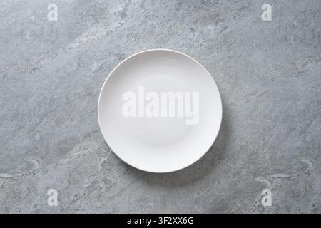 Empty white ceramic plate on gray stone background with copy space. Minimal table setting for food presentation and menu design. Stock Photo