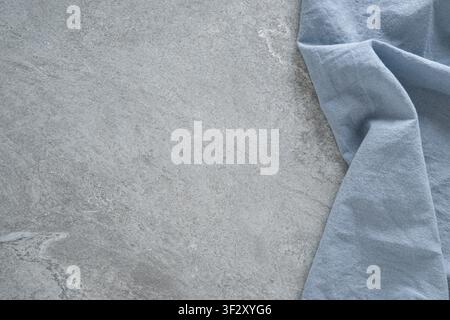 Soft blue linen fabric on gray stone background with copy space. Minimal textile backdrop for kitchen and home styling. Stock Photo