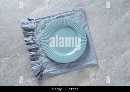 Empty light blue ceramic dinner plate on soft linen napkin over gray stone background. Minimal table setting with copy space for food, menu or recipe Stock Photo