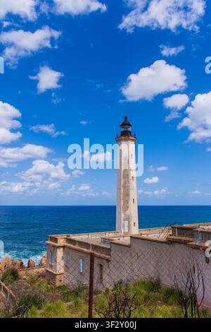 Historic weathered white lighthouse tower standing against a blue sky with clouds and the sea in Béjaïa, Algeria. Stock Photo