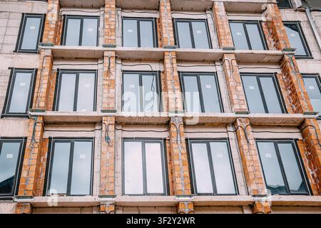 Building facade featuring new windows, concrete slabs, and exposed brick columns, representing ongoing construction and urban development Stock Photo