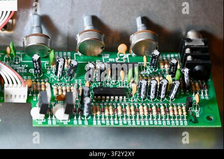Close-Up of Printed Circuit Board with Capacitors, Resistors, and Potentiometers. High quality photoDetailed macro shot of a green printed circuit board (PCB) showing electronic components including electrolytic capacitors, resistors, potentiometers, microchips, and wiring. Ideal for concepts of hardware engineering, electronics repair, audio equipment manufacturing, and technology design. Stock Photo