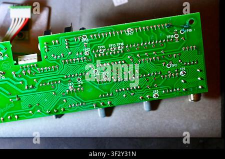 Technician Testing Circuit Board Tracks with Multimeter Probe Close Up. High quality photoMacro shot of the backside of a green printed circuit board (PCB) showing soldered joints, copper tracks, and marked test points (TP). A technician uses a probe tool to test connections and diagnose electrical faults. Perfect for concepts of electronics diagnostics, hardware repair, soldering quality inspection, and engineering. Stock Photo