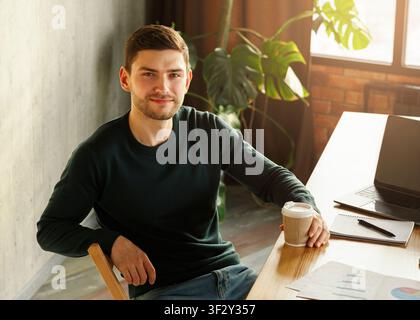 Guy At Laptop Holding Coffee Sitting At Workdesk In Office Stock Photo