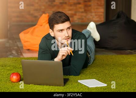 Guy Using Laptop Thinking Lying On Floor In Coworking Workspace Stock Photo