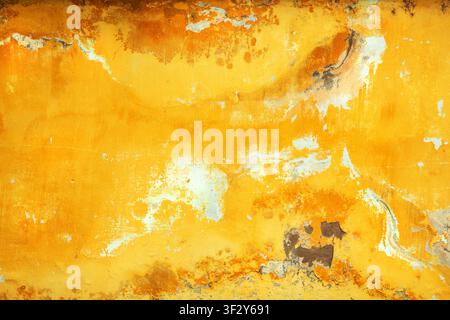 Full-frame texture of an old, weathered yellow concrete wall with peeling paint, cracks, and exposed plaster spots as background. Stock Photo