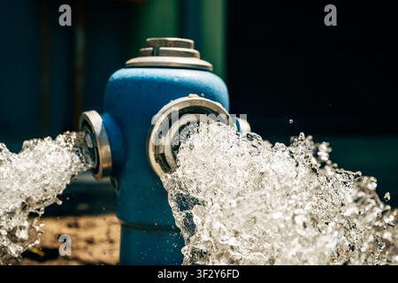 Blue fire hydrant flushing high-pressure water from open side valves into street gutter. Municipal water supply, infrastructure maintenance and public Stock Photo