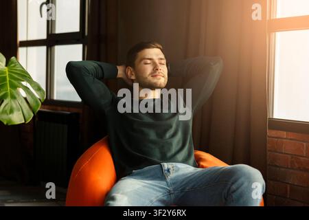 Relaxed Millennial Guy Sitting On Beanbag Chair In Modern Interior Stock Photo
