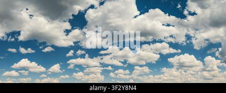 Wide panoramic view of a vivid blue sky filled with scattered white and grey cumulus clouds in bright daylight. Stock Photo