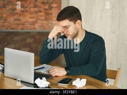 Tired Young Man Having Headache Sitting At Laptop In Office Stock Photo