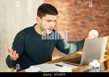 Emotional Worker Looking At Laptop Having Problem Sitting In Office Stock Photo