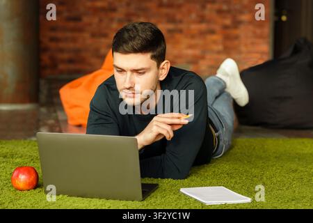 Millennial Guy Using Laptop Lying On Floor At Home Stock Photo