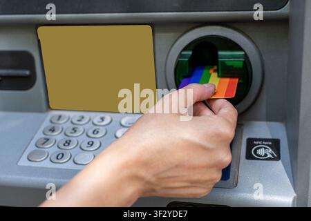 Hand inserting rainbow credit card into atm machine Stock Photo