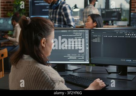 Software programmer writes database code in front of multiple screens showing artificial intelligence algorithms, while colleagues collaborate on cloud computing work. Stock Photo