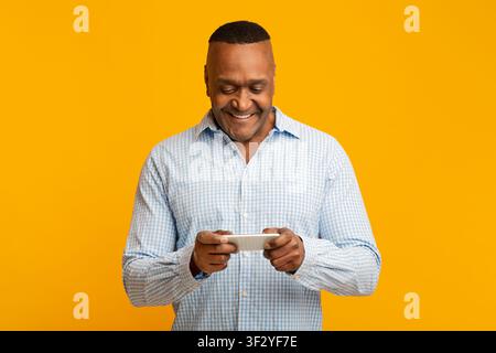 Middle aged african man playing video games on cellphone Stock Photo