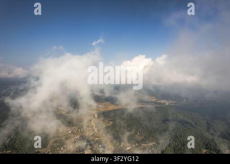 Aerial view of the mountainous landscape of Andirin with scattered houses, dense forests, and fluffy white clouds drifting over the terrain in Andirin Stock Photo