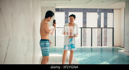 Gay couple enjoying poolside leisure, taking pictures, and sharing happy moments Stock Photo