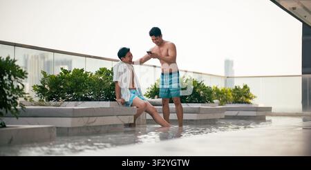 Two asian gay men enjoying a summer day at a modern rooftop pool Stock Photo