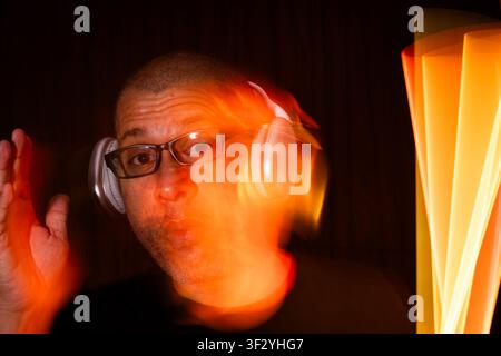 Man enjoying music on headphones with dynamic orange light streaks, creating a feeling of movement Stock Photo