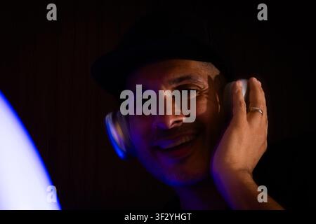 Happy man wearing headphones and hat in glowing neon light Stock Photo