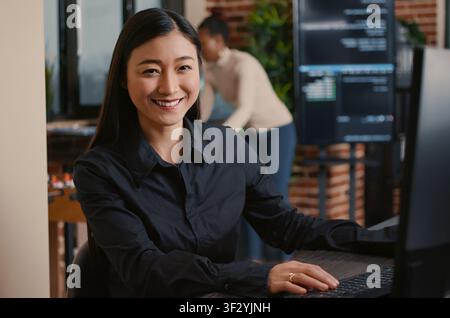 Asian software developer smiling and resuming work typing code on computer keyboard sitting at desk in big data office, with artificial intelligence and big data. Stock Photo