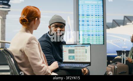 Diverse coworkers reviewing data reports on laptop in business lounge, examining situation for business briefing. Man and woman associates preparing for international meeting airplane travel. Stock Photo
