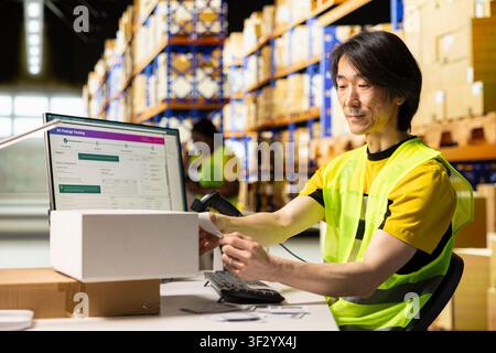 Asian employee applying adhesive label with tracking number on packages, manages labeling and packaging operations in a distribution hub. Printing barcodes tags and sticking them on boxes. Stock Photo