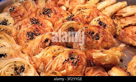 A close-up of a tray filled with golden brown, freshly baked Turkish savory pastries topped with black sesame seeds. Stock Photo