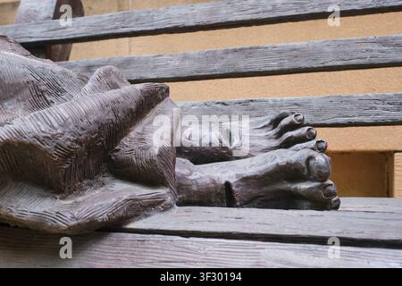 Bronze sculpture of a homeless man on a bench, covered in a blanket. With Christ-like stigmata. At St James Anglican Church in Sydney, Australia. Stock Photo
