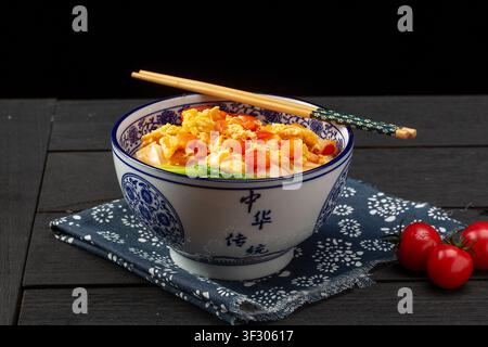 A bowl of homemade tomato egg noodles served with green vegetables and side dishes on a wooden tray. Stock Photo