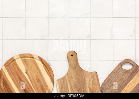 Three wooden cutting boards with different shapes and wood grains on a light tiled background, kitchen utensils and cooking preparation Stock Photo